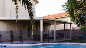 Un pati exterior cobert amb piscina, envoltat per una tanca i palmeres.