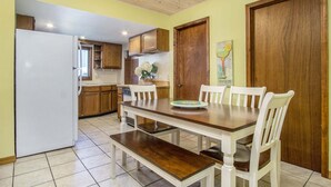 A kitchen with wooden cabinets, a white refrigerator, and a dining table with white chairs. - Driftwood: Downtown Saugatuck Home, Walk to Shops & Restaurants, Dog-Friendly (Saugatuck)