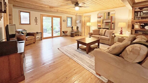 A spacious living room with wooden floors and ceiling, a large sofa set, a coffee table, and a bookshelf. - Hillcrest: Downtown, Fire Pit, Fenced in Yard, Pet Friendly (Saugatuck)