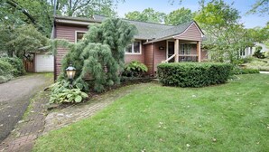 A two-story house with a front porch, a garage, and a well-maintained lawn. - Hillcrest: Downtown, Fire Pit, Fenced in Yard, Pet Friendly (Saugatuck)