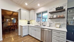 A modern kitchen with white cabinetry, a stainless steel dishwasher, and a window above the sink. - Hillcrest: Downtown, Fire Pit, Fenced in Yard, Pet Friendly (Saugatuck)