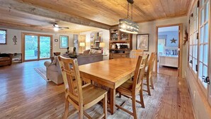 A spacious living area with a wooden dining table, chairs, and a sofa. There is a kitchen area with a hanging light fixture. - Hillcrest: Downtown, Fire Pit, Fenced in Yard, Pet Friendly (Saugatuck)