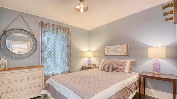 A bedroom with a bed, bedside tables, a dresser, a mirror, and a ceiling light.