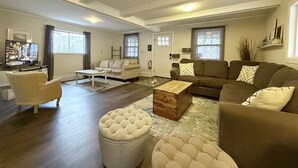 Ein geräumiges Wohnzimmer mit einer Couch, einem Hocker, einem Couchtisch, einem Fernseher und einem Kamin.