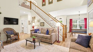 Una sala de estar amplia con una escalera, un sofá, un sillón y una televisión.