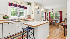 Una cocina con una isla de madera, armarios blancos y un valance rojo y azul.