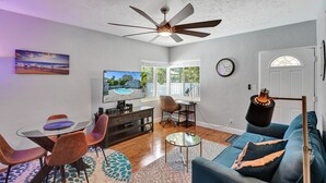 Un salon avec un ventilateur de plafond, un téléviseur, une table à manger avec des chaises, un canapé et une horloge au mur.