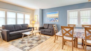 A living room with a sofa, coffee table, and dining table with chairs. - Malabar: Downtown Saugatuck Cottage, Fire Pit, Pet Friendly, Sun Room, Porch (Saugatuck)