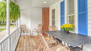 A covered porch with a table and chairs, a brick chimney, and blue shutters. - Malabar: Downtown Saugatuck Cottage, Fire Pit, Pet Friendly, Sun Room, Porch (Saugatuck)