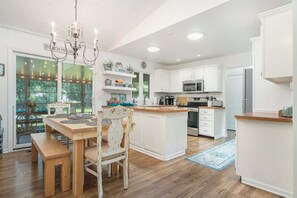 A kitchen with white cabinets, a wooden dining table, and a chandelier.