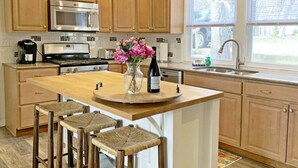 Una cocina con gabinetes de madera, una isla central con taburetes, un microondas, una estufa y un fregadero.