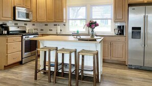 Una cocina con armarios de madera, un refrigerador de acero inoxidable, un microondas, una estufa y un ventanal grande.