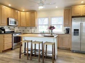 A kitchen with wooden cabinets, a stainless steel refrigerator, a microwave, a stove, and a large window.