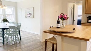 Una cocina moderna con una isla de madera, un comedor con sillas blancas y un jarrón con flores.