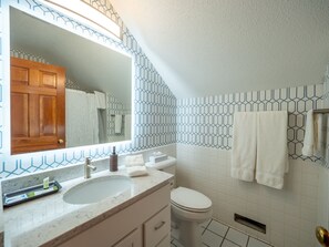 A bathroom with a large mirror, a sink, a toilet, and a shower area.