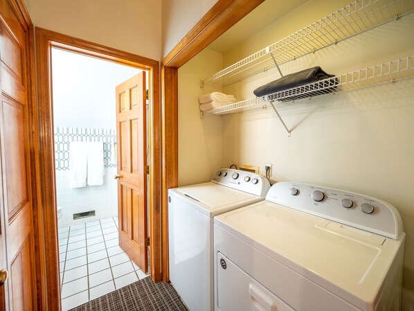 A laundry room with two white washing machines, a drying rack, and a door leading to a tiled hallway.