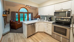 Una cocina moderna con armarios blancos, electrodomésticos de acero inoxidable, lavavajillas y un amplio ventanal con vistas a un paisaje verde.