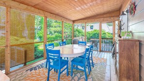A covered patio with a round table and blue chairs, large windows, and a view of greenery. - Lad and Fellow: Downtown Saugatuck Home Near Shops & Restaurants, Pet-Friendly (Saugatuck)