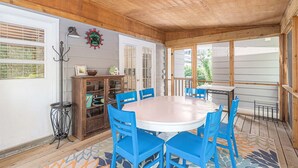 A covered patio with a round table and blue chairs, wooden ceiling, and a decorative wall clock. - Lad and Fellow: Downtown Saugatuck Home Near Shops & Restaurants, Pet-Friendly (Saugatuck)