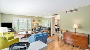 A living room with a sofa, a coffee table, a TV, and a dining area with a chandelier. - Lad and Fellow: Downtown Saugatuck Home Near Shops & Restaurants, Pet-Friendly (Saugatuck)