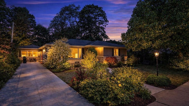 A two-story house with a covered patio and a well-lit garden at dusk. - Lad and Fellow: Downtown Saugatuck Home Near Shops & Restaurants, Pet-Friendly (Saugatuck)