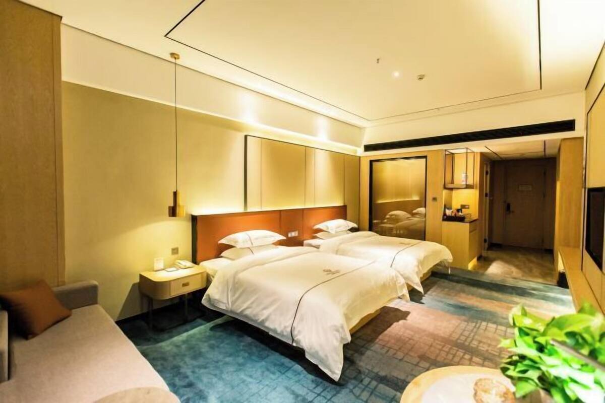 Een hotelkamer met twee bedden, een bureau, een stoel, een nachtkastje, een spiegel en een kleine plant.