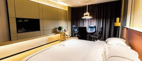 A modern hotel room with a large bed, a flat-screen TV, a desk with a chair, and a large window with curtains.