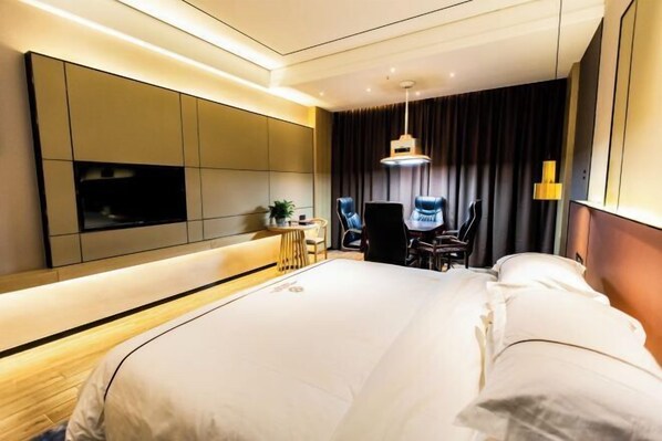 Habitación de hotel moderna con una cama grande, un televisor de pantalla plana, un escritorio con una silla y un ventanal con cortinas.