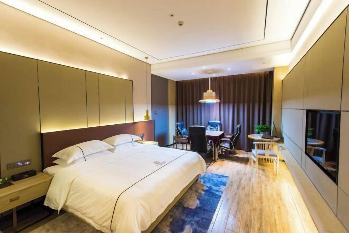 Een moderne hotelkamer met een groot bed, een bureau met twee stoelen, een kleine tafel en een televisie.