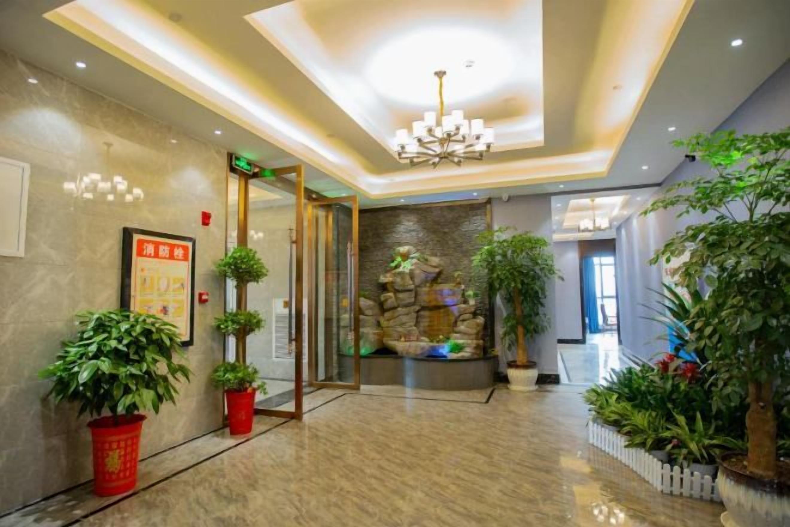 A hotel lobby with a marble floor, a chandelier, and potted plants.