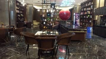 A well-lit library with bookshelves, a large red sculpture, and a dining area with wicker chairs and a glass table.