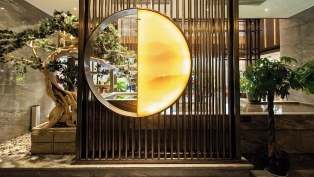 A modern interior with a circular mirror reflecting a warm interior, surrounded by vertical wooden slats and a sculptural tree installation. - Huarong Mingwei International Hotel (Huarong)