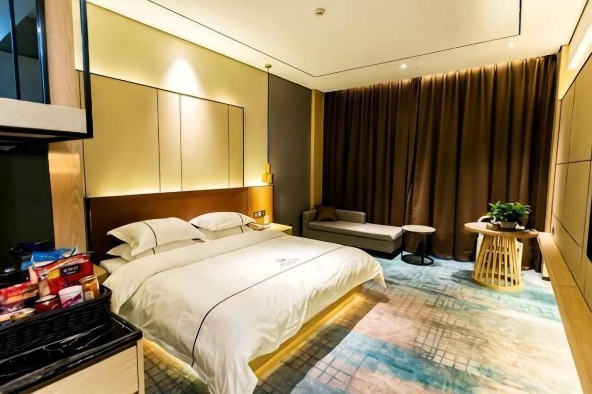 Hotelkamer met een bed, nachtkastje, lamp, zithoek en een klein rond tafeltje met een plant.