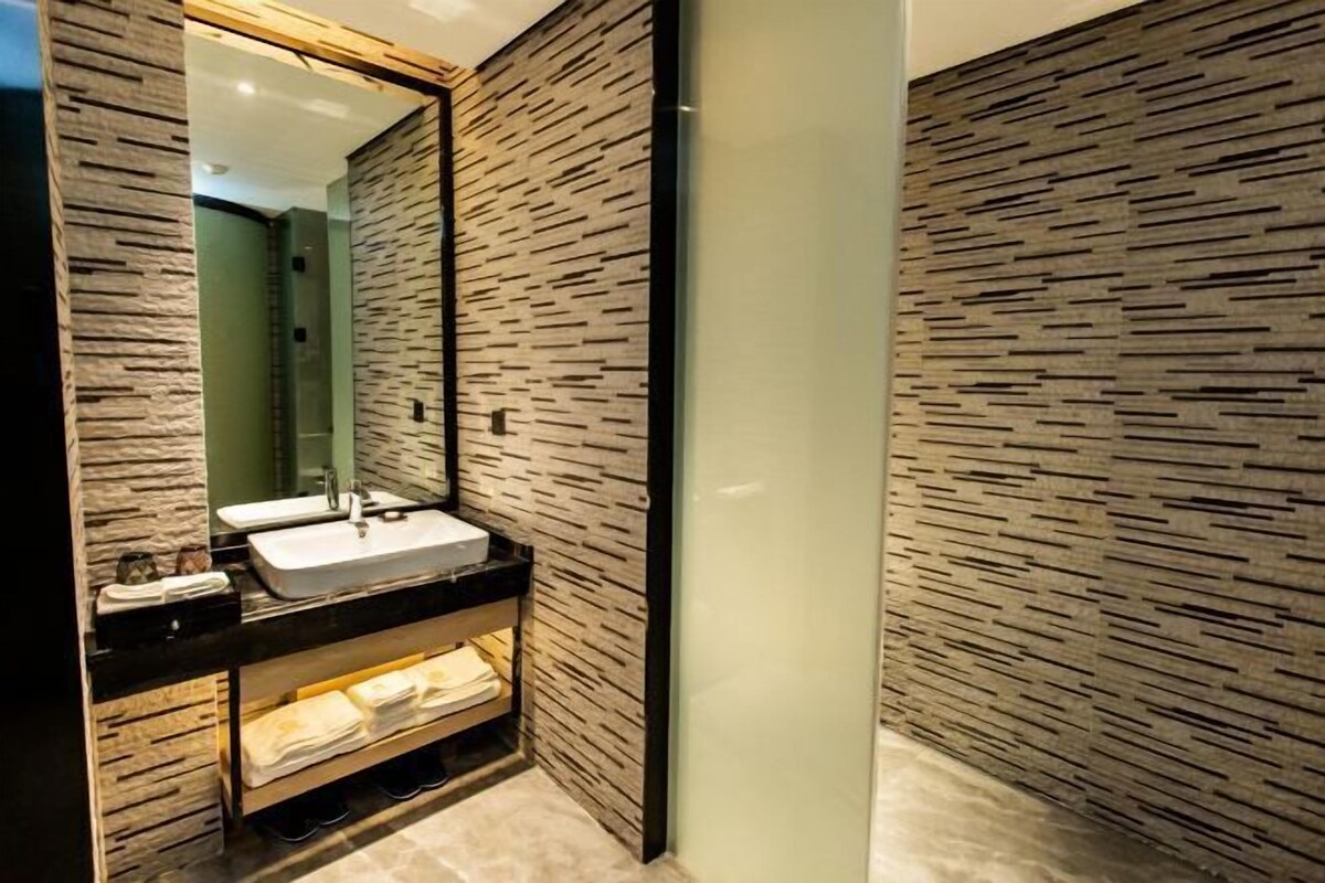 Un baño moderno con pared de textura de piedra, un espejo grande, un lavamanos y un estante con toallas.