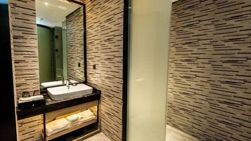 Un baño moderno con pared de textura de piedra, un espejo grande, un lavamanos y un estante con toallas.