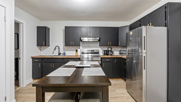 A modern kitchen with dark cabinets, stainless steel appliances, and a wooden dining table. - Bo's Bnbs Unit 2 Downtown Exeter (Exeter)
