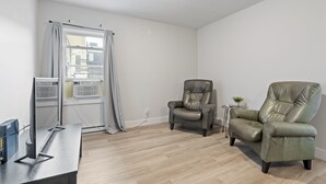 A modern living room with a flat-screen TV, two leather armchairs, a small side table with a plant, and a window with curtains. - Bo's Bnbs Unit 2 Downtown Exeter (Exeter)