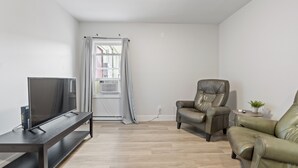 A modern living room with a flat-screen TV on a dark wooden TV stand, a leather armchair, a sofa, and a small table with a plant. - Bo's Bnbs Unit 2 Downtown Exeter (Exeter)