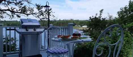 Eine Terrasse mit Grill, Tisch und Stühlen und Blick auf den See.