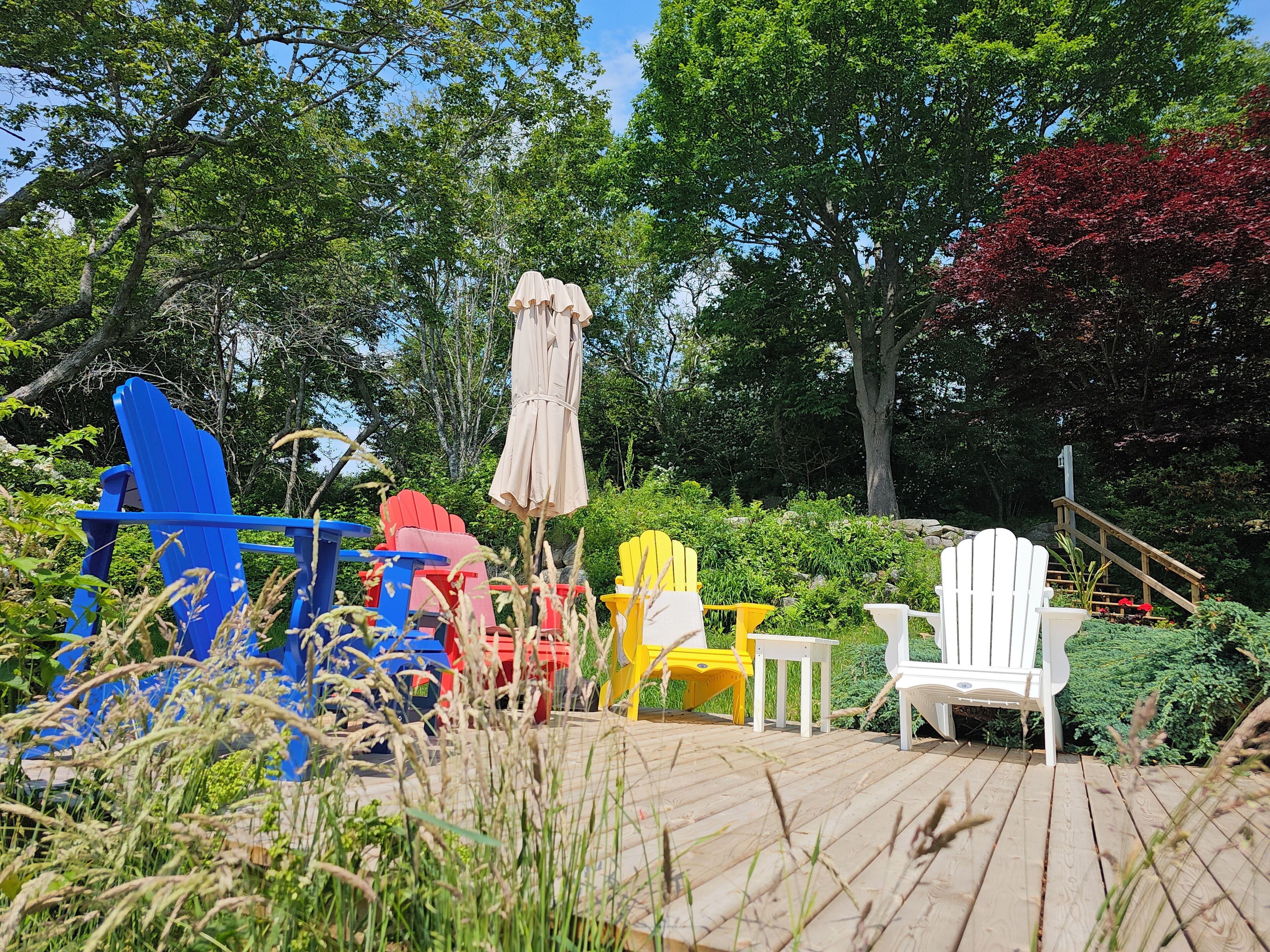 A wooden deck with colorful Adirondack chairs and a white chair.