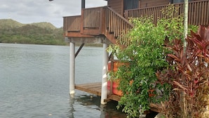 A wooden structure with a balcony over water, surrounded by greenery.