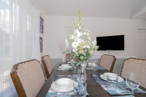 Et spisebord dækket med hvide tallerkener, glas og en vase med hvide blomster.