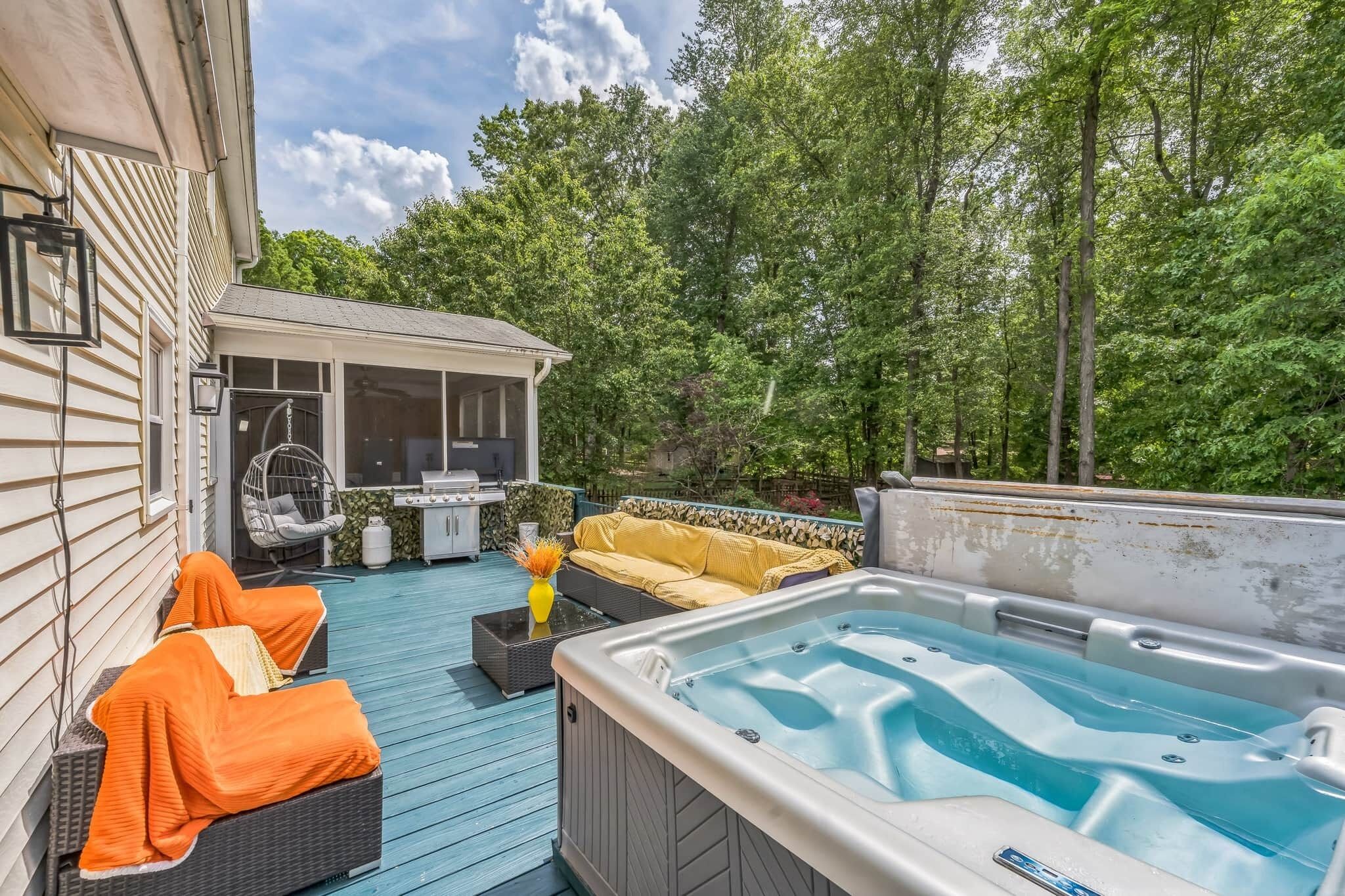 Patio trasero con jacuzzi, mobiliario exterior y una zona cubierta con parrilla.