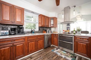 A kitchen with wooden cabinets, stainless steel appliances, and a window with blinds.