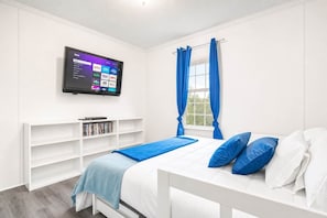 A bedroom with a bed, a TV mounted on the wall, a window with curtains, and a bookshelf. - Parking for 75+ Travel Workers Welcome (Rockingham County)
