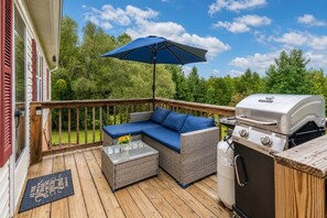Una terraza con un sofá de mimbre, una mesa de centro de cristal, una parrilla y un parasol azul.