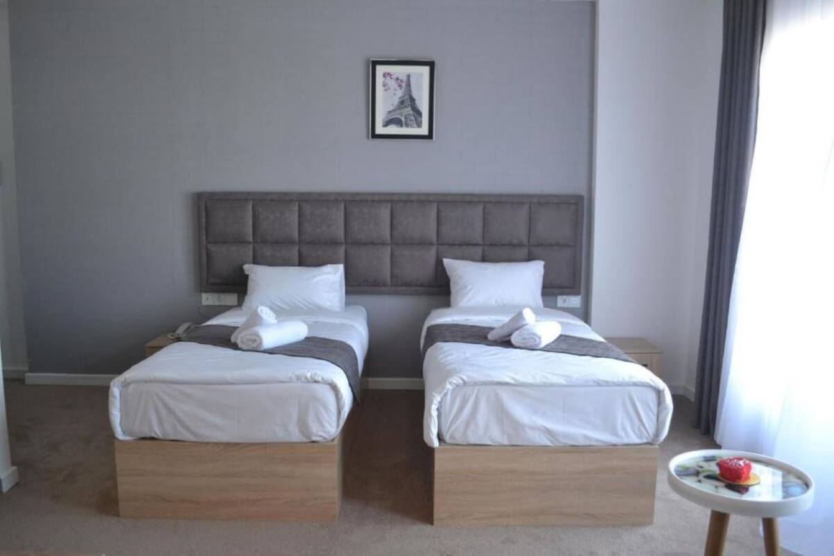 Ein Hotelzimmer mit zwei Betten, einem grauen Kopfteil und einem kleinen Tisch mit Obst.