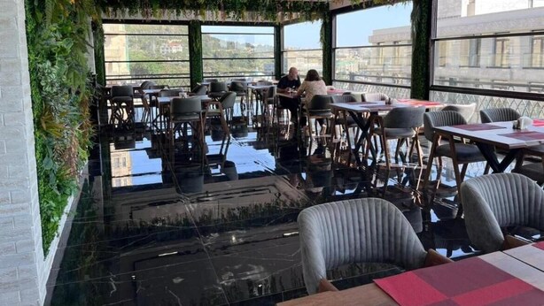 A restaurant with a glass floor, tables, chairs, and greenery. - Hotel Madinah (Baku)