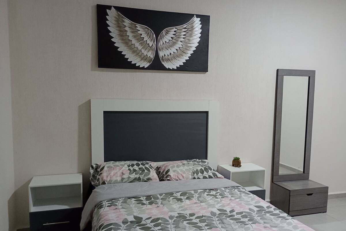 Een slaapkamer met een bed, nachtkastje, kaptafel, spiegel en een kunstwerk aan de muur.