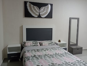 Une chambre à coucher comprenant un lit, une table de chevet, une commode, un miroir et une œuvre d’art murale.
